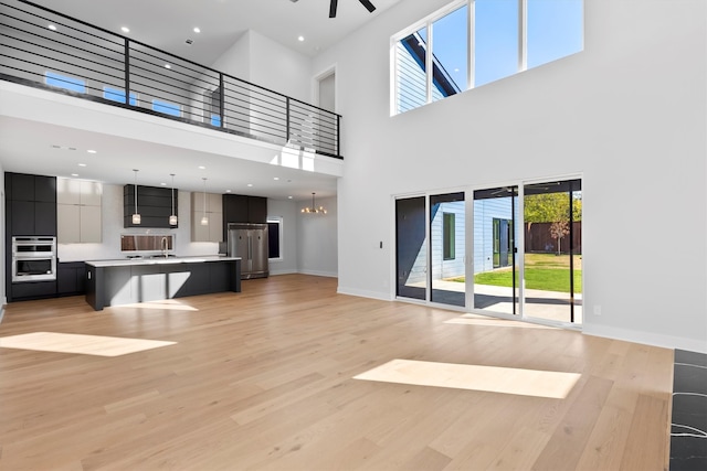 unfurnished living room featuring ceiling fan with notable chandelier, a towering ceiling, and light hardwood / wood-style flooring