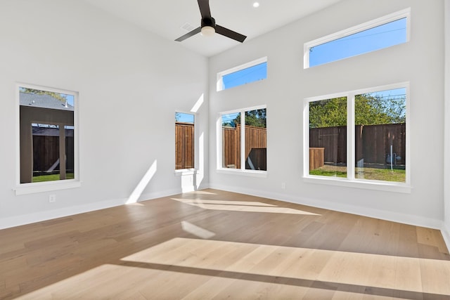 unfurnished room with ceiling fan, wood-type flooring, and a towering ceiling