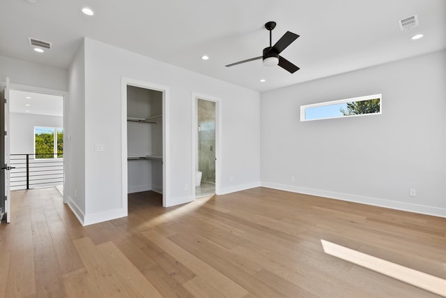 unfurnished bedroom with ensuite bathroom, light hardwood / wood-style flooring, ceiling fan, a spacious closet, and a closet