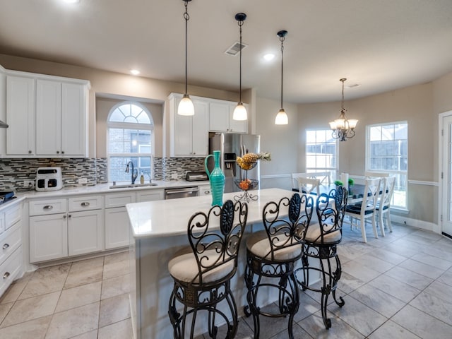 kitchen featuring sink, appliances with stainless steel finishes, decorative light fixtures, a kitchen island, and white cabinetry