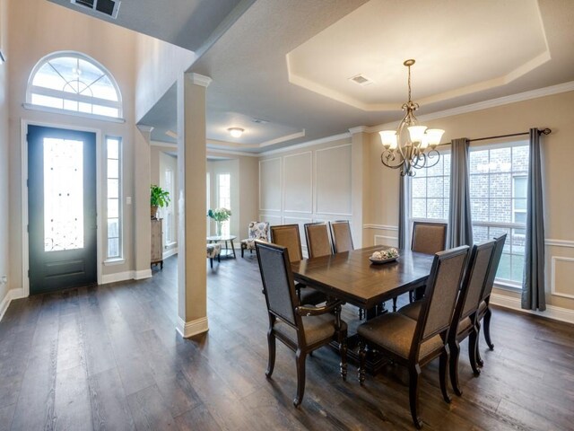 dining area featuring dark hardwood / wood-style floors, decorative columns, a tray ceiling, and a notable chandelier