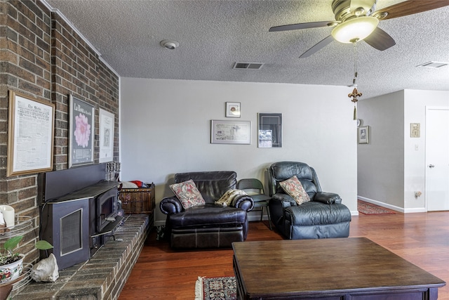 living room featuring a wood stove, dark hardwood / wood-style floors, ceiling fan, a textured ceiling, and brick wall