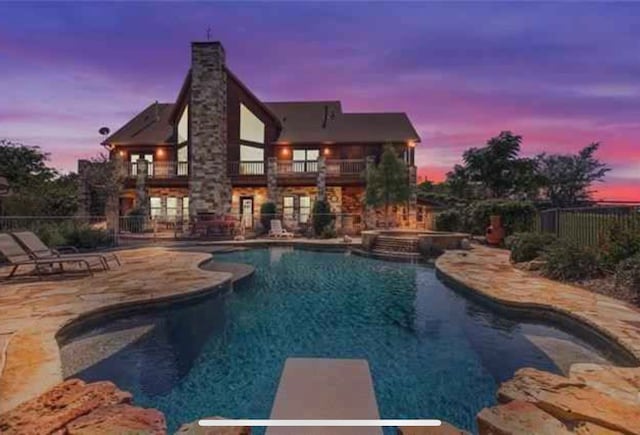 pool at dusk with a diving board, a patio area, and an in ground hot tub