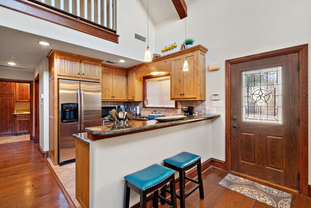 kitchen with hardwood / wood-style floors, a breakfast bar, hanging light fixtures, stainless steel fridge with ice dispenser, and kitchen peninsula