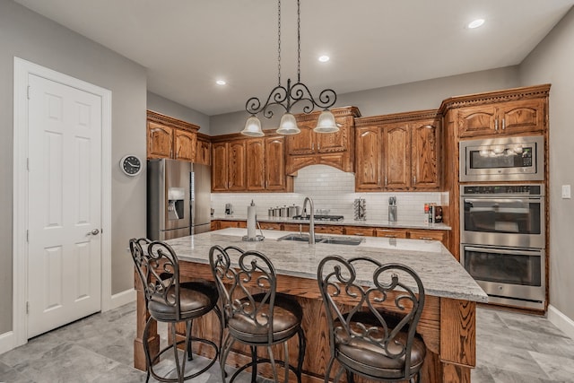 kitchen featuring stainless steel appliances, hanging light fixtures, a center island with sink, and backsplash