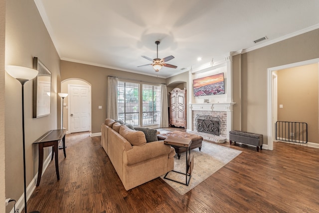 living room featuring a fireplace, dark wood-type flooring, ornamental molding, and ceiling fan