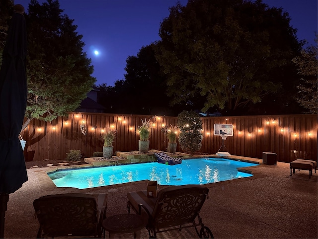 pool at night featuring a patio area