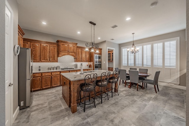 kitchen featuring pendant lighting, tasteful backsplash, a kitchen island with sink, stainless steel appliances, and light stone countertops