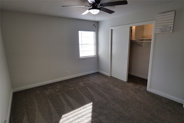 unfurnished bedroom featuring dark colored carpet, a walk in closet, a closet, and ceiling fan