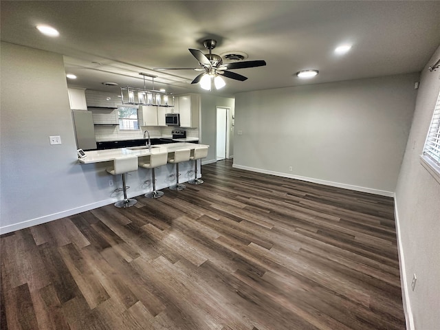 kitchen with dark wood-type flooring, stainless steel appliances, a kitchen breakfast bar, pendant lighting, and white cabinets