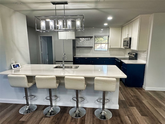 kitchen featuring stainless steel appliances, blue cabinets, sink, decorative light fixtures, and white cabinetry