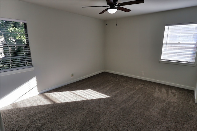 spare room with a wealth of natural light, ceiling fan, and dark colored carpet