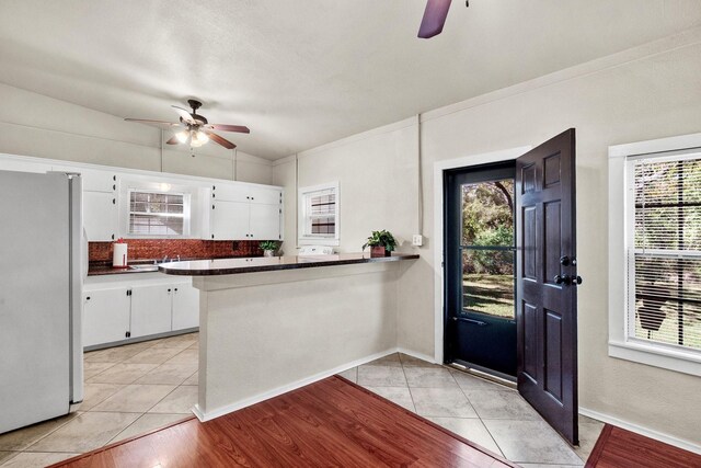 kitchen with white cabinets, a wealth of natural light, kitchen peninsula, and white fridge