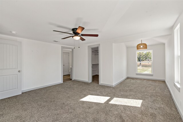 unfurnished bedroom featuring a spacious closet, a closet, ceiling fan, and light carpet