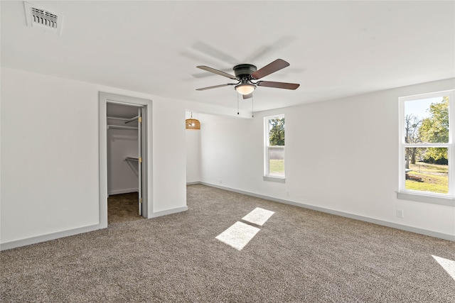 unfurnished bedroom with a closet, a walk in closet, carpet floors, and ceiling fan