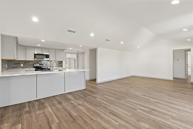 kitchen with backsplash, vaulted ceiling, light hardwood / wood-style floors, kitchen peninsula, and stainless steel appliances