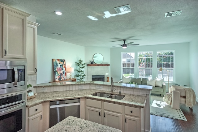 kitchen featuring sink, hardwood / wood-style flooring, ceiling fan, appliances with stainless steel finishes, and light stone counters