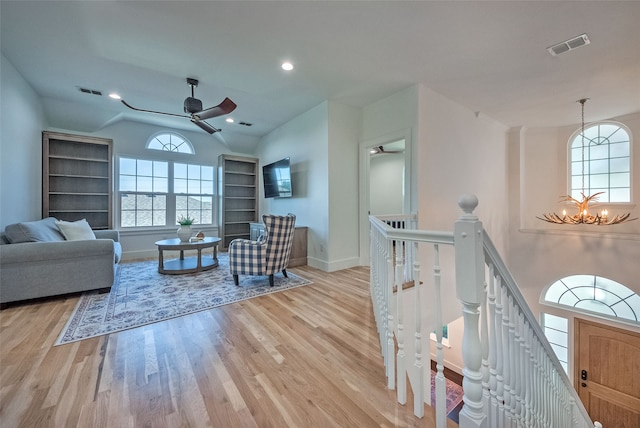 living room with ceiling fan with notable chandelier, light hardwood / wood-style flooring, and lofted ceiling