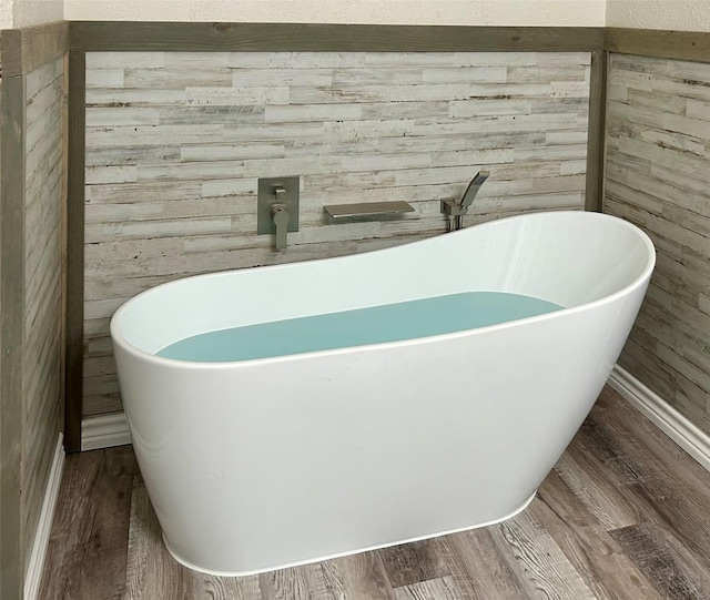 bathroom with a washtub, wood-type flooring, and wooden walls