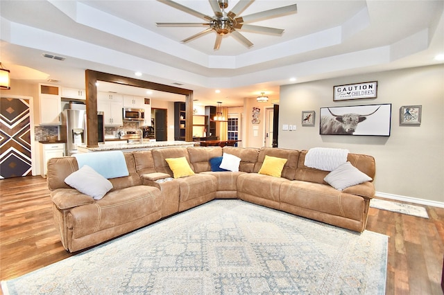 living room featuring a raised ceiling, ceiling fan, and light hardwood / wood-style floors