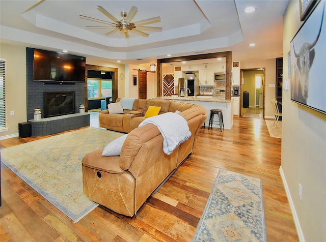 living room with a brick fireplace, ceiling fan, a barn door, and a tray ceiling