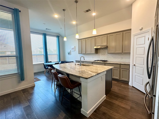 kitchen with light stone countertops, dark wood-type flooring, sink, pendant lighting, and a center island with sink