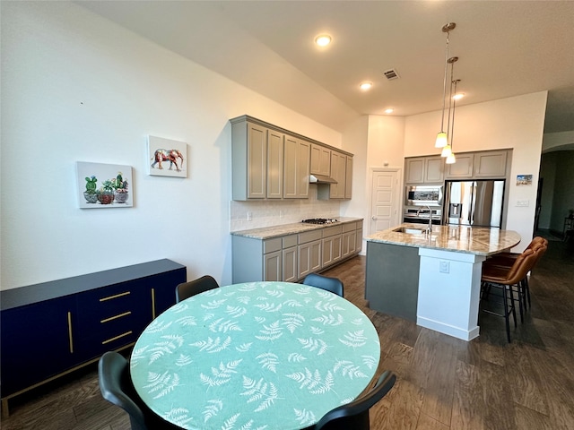 kitchen featuring gray cabinetry, stainless steel appliances, dark wood-type flooring, a center island with sink, and hanging light fixtures