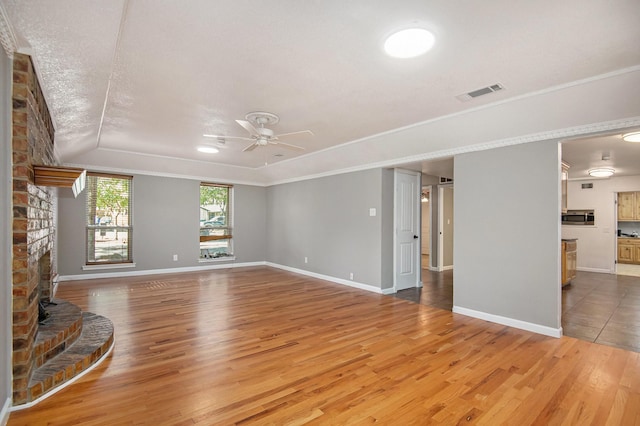 unfurnished living room featuring crown molding, ceiling fan, wood-type flooring, and a fireplace