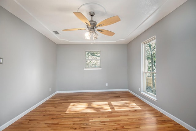 empty room featuring ceiling fan, a wealth of natural light, and light wood-type flooring