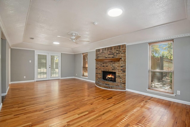 unfurnished living room featuring crown molding, a textured ceiling, a brick fireplace, french doors, and light wood-type flooring