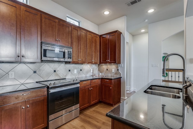 kitchen featuring appliances with stainless steel finishes, backsplash, sink, dark stone countertops, and light hardwood / wood-style floors