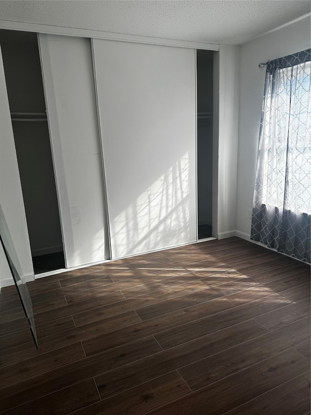 unfurnished bedroom featuring a textured ceiling, dark wood-type flooring, and a closet