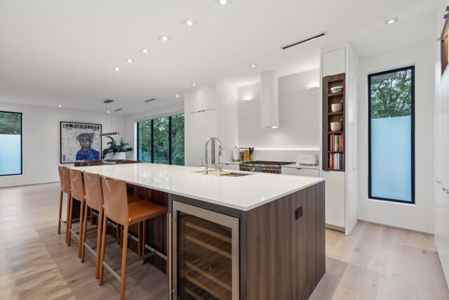 kitchen featuring white cabinetry, sink, beverage cooler, a center island with sink, and light wood-type flooring