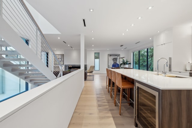 kitchen with sink, wine cooler, light hardwood / wood-style flooring, a breakfast bar, and white cabinets