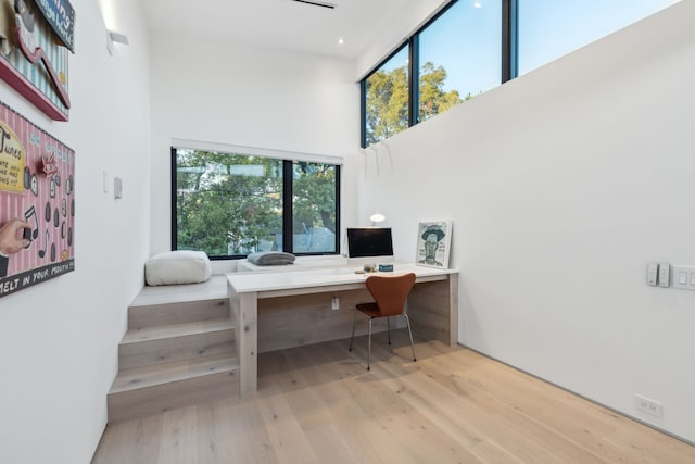 home office featuring a towering ceiling, built in desk, and light hardwood / wood-style flooring