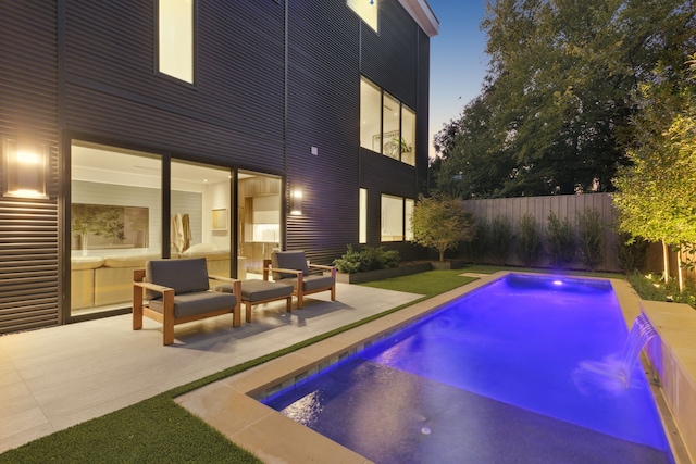 pool at dusk featuring pool water feature, a patio, and an outdoor living space