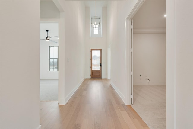 entryway featuring a towering ceiling, a healthy amount of sunlight, a chandelier, and light hardwood / wood-style floors