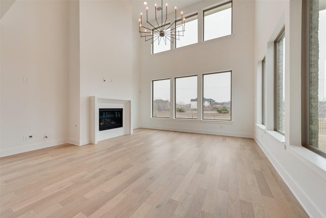 unfurnished living room with a towering ceiling, a chandelier, and light hardwood / wood-style floors