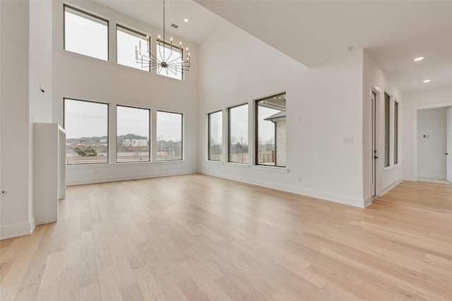 unfurnished living room featuring a high ceiling, a notable chandelier, and light hardwood / wood-style flooring