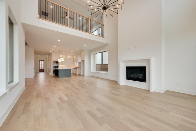 unfurnished living room with sink, light hardwood / wood-style flooring, a chandelier, and a high ceiling