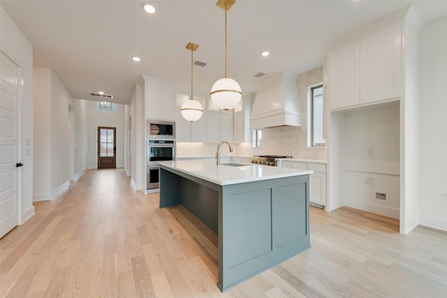 kitchen featuring sink, white cabinetry, a kitchen island with sink, stainless steel microwave, and custom exhaust hood