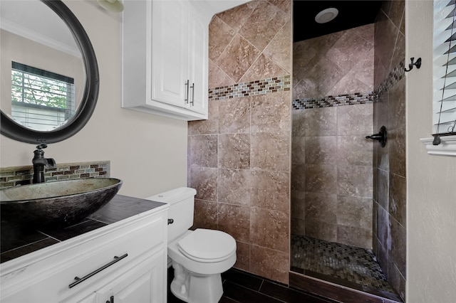 bathroom with toilet, a tile shower, crown molding, and vanity