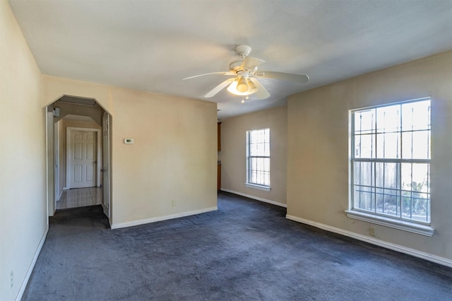 spare room featuring a ceiling fan, arched walkways, dark carpet, and baseboards