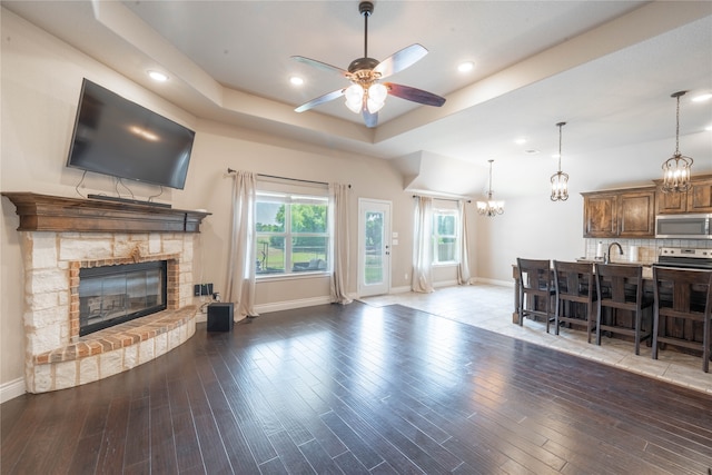 living room with a tray ceiling, ceiling fan, a fireplace, and dark wood-type flooring