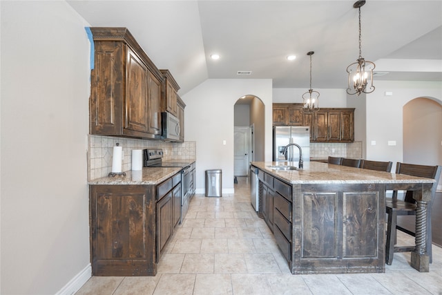 kitchen featuring a center island with sink, sink, appliances with stainless steel finishes, light stone counters, and a breakfast bar area