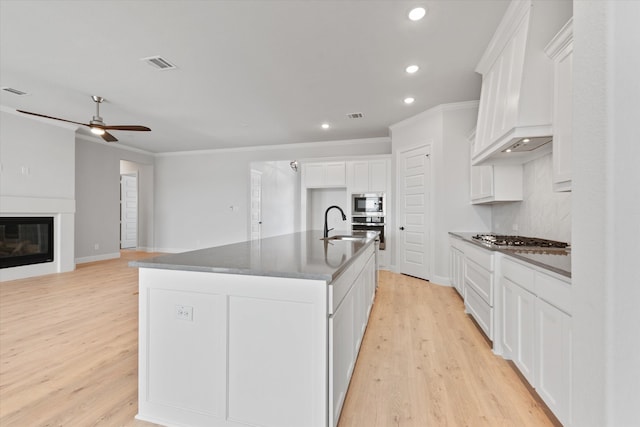 kitchen with a center island with sink, light wood-type flooring, ornamental molding, white cabinetry, and stainless steel appliances