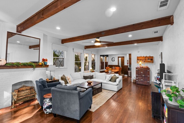 living room featuring beam ceiling, ceiling fan, dark wood-type flooring, and a brick fireplace