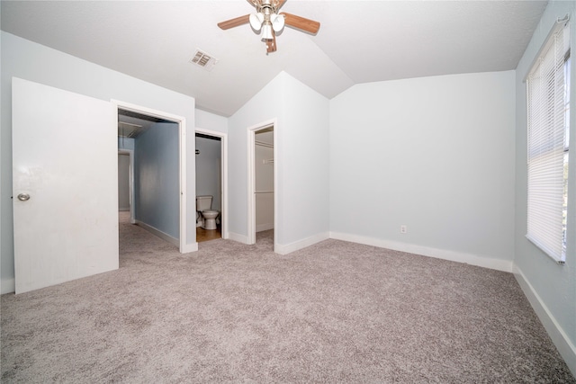 unfurnished bedroom with carpet, a walk in closet, ensuite bath, vaulted ceiling, and ceiling fan