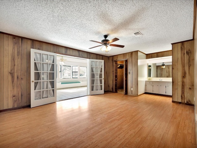 unfurnished living room with french doors, light wood-type flooring, and wood walls