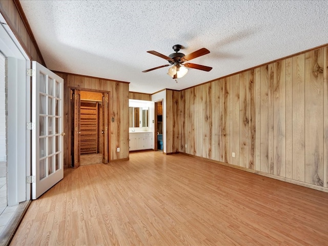 interior space featuring ensuite bathroom, wooden walls, light hardwood / wood-style flooring, ceiling fan, and a closet